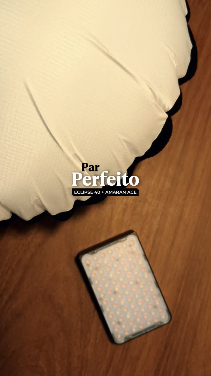 Mão segurando um painel de LED de bolso sobre mesa de madeira, sob luz difusa.